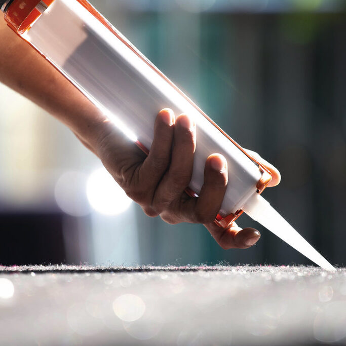Men's hand uses silicone adhesive with a glue gun to repair worn windows.